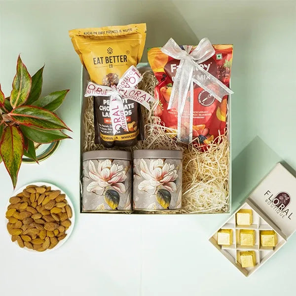 gift hamper of aglaonema pink diamond plant with eat better snacks and dry flowers front view