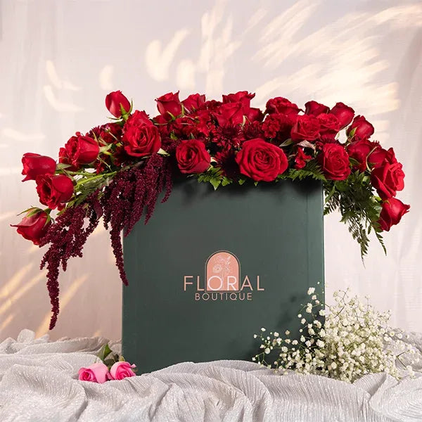 a large green box filled with red roses celosia and chrysanthemums front view