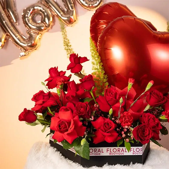 red rose and carnation arrangement in a box with two heart balloons front view
