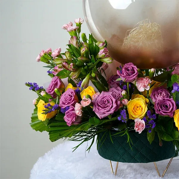 green box with stand purple yellow roses spray carnations clear balloon. close up view