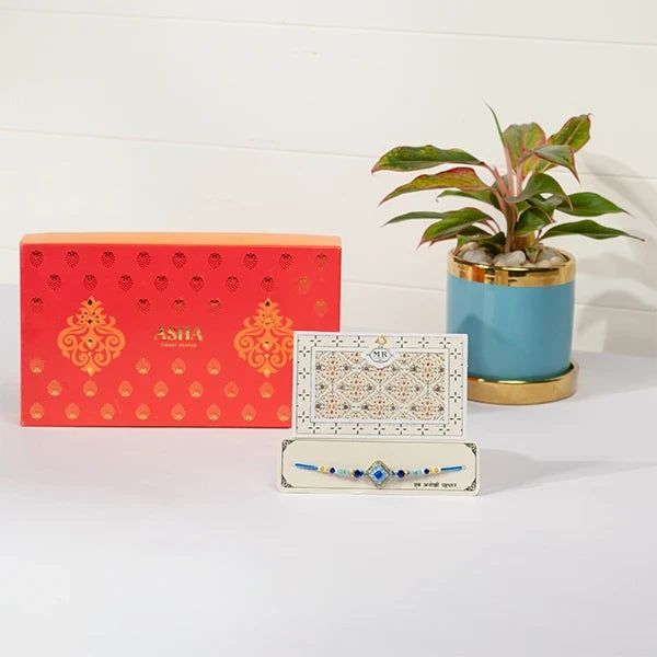azure rakhi hamper with asha sweet mix aglaonema in blue pot front view