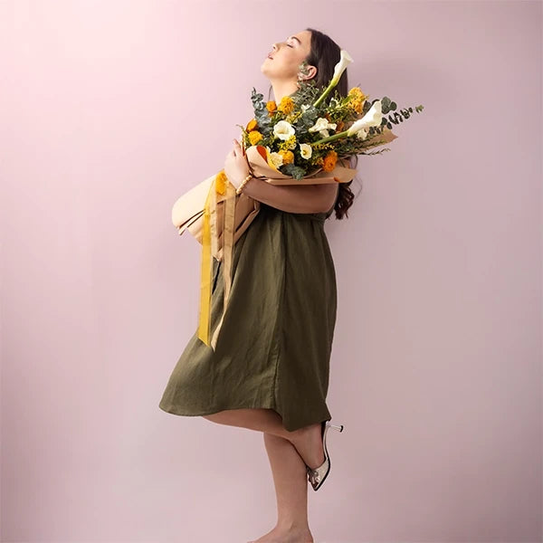 lily bouquet with yellow celosia white carnations wrapped in brown paper lifestyle view
