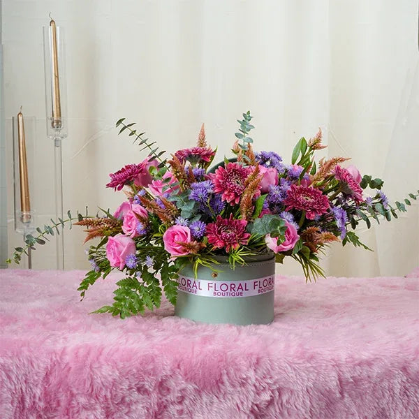 a round leather box filled with a mix of revival roses and mini gerberas front view
