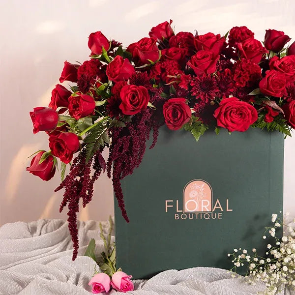 a large green box filled with red roses celosia and chrysanthemums close up view