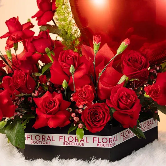 red rose and carnation arrangement in a box with two heart balloons side view