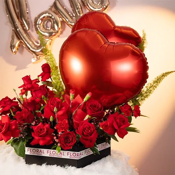 red rose and carnation arrangement in a box with two heart balloons close up view